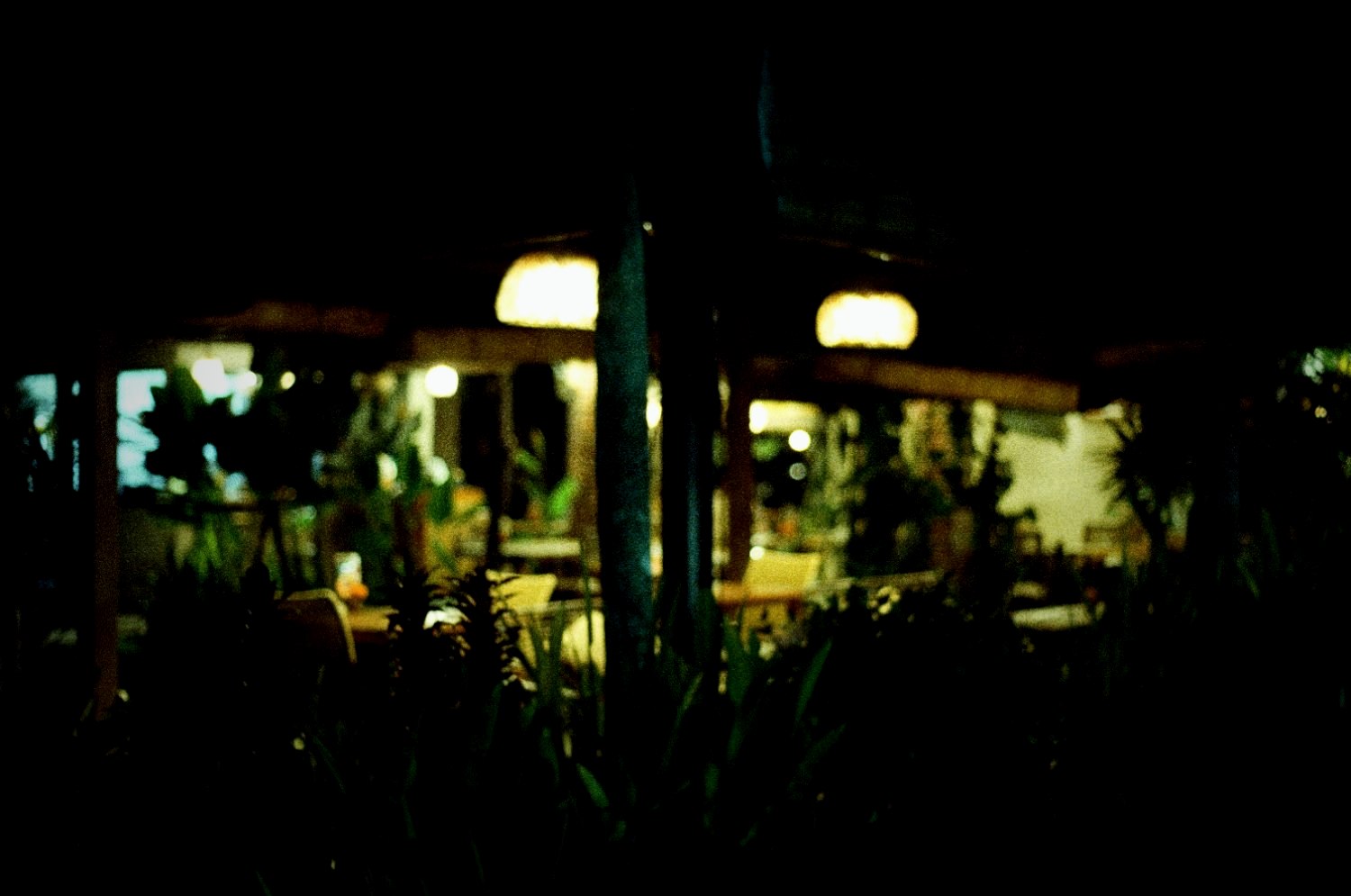 A warung lit at night, seen across dark grass