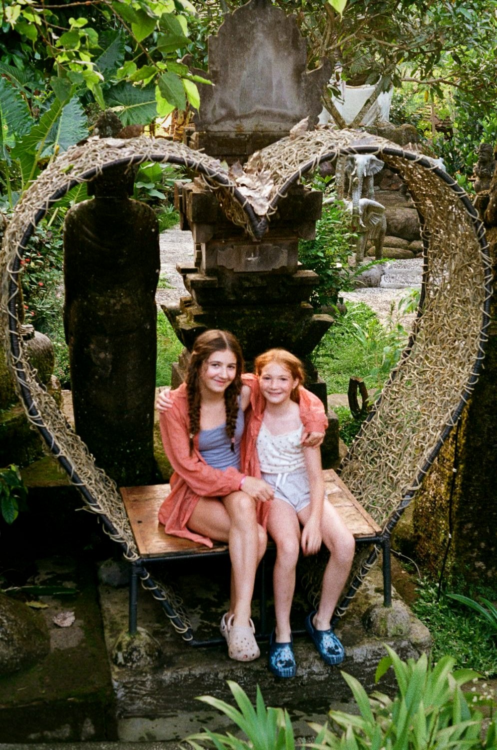Two girls in a heart-shaped rattan swing in a garden