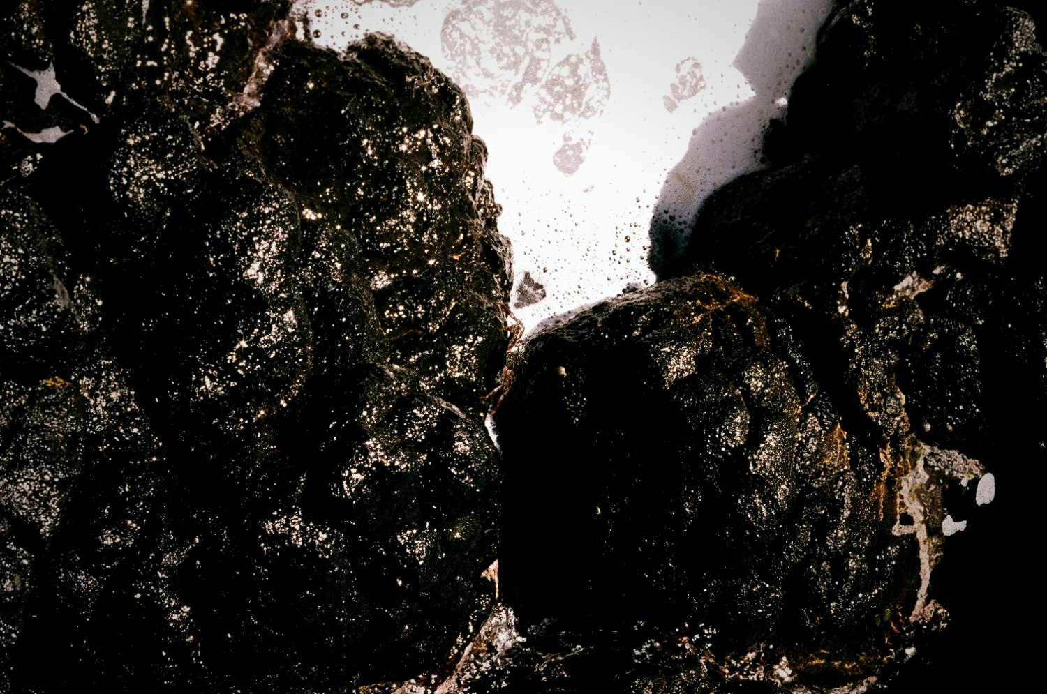Black volcanic rock against bright surf