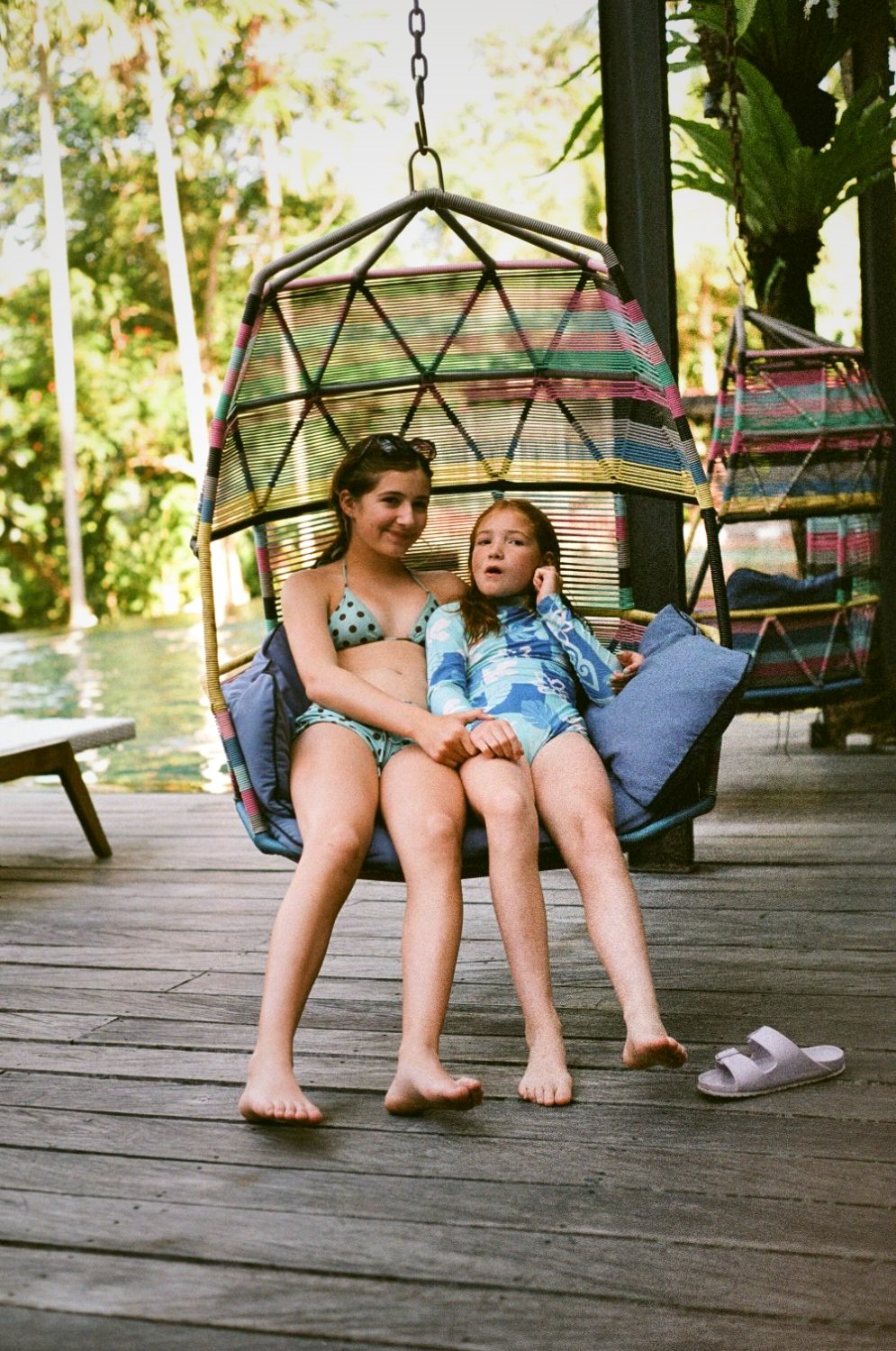 Two children sharing a hanging swing chair on a deck