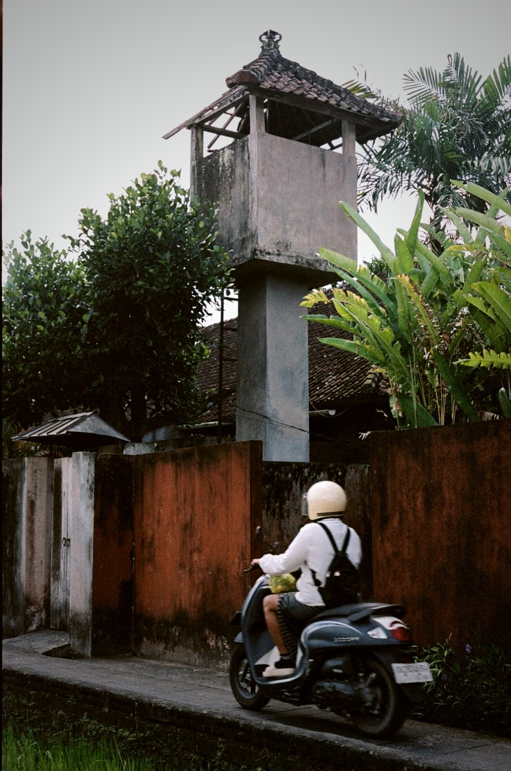 A tall stone shrine tower above a villa wall at dusk